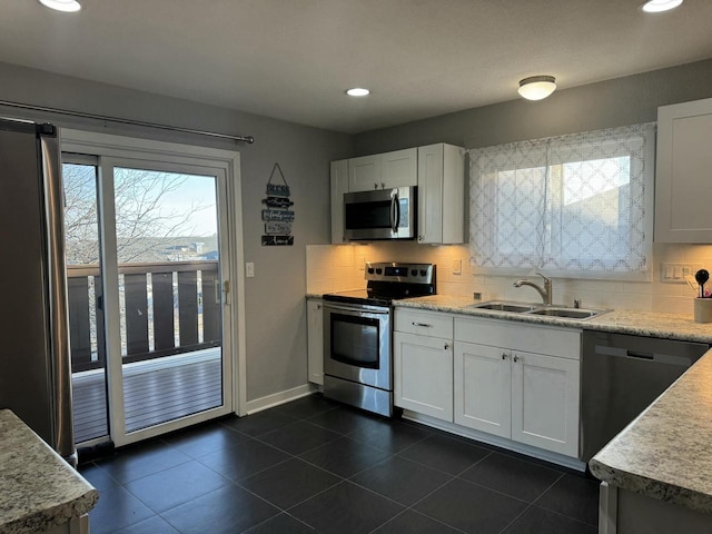 kitchen featuring dark tile patterned flooring, a sink, tasteful backsplash, stainless steel appliances, and white cabinets