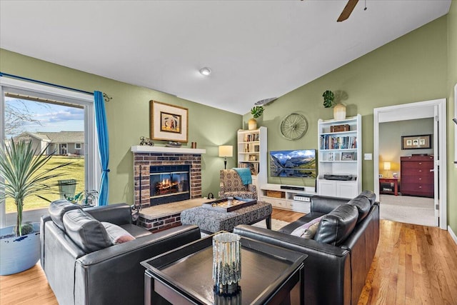 living area with a ceiling fan, lofted ceiling, wood finished floors, and a fireplace