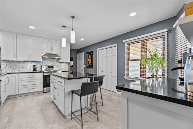 kitchen with dark countertops, backsplash, under cabinet range hood, stainless steel range with electric stovetop, and white cabinets