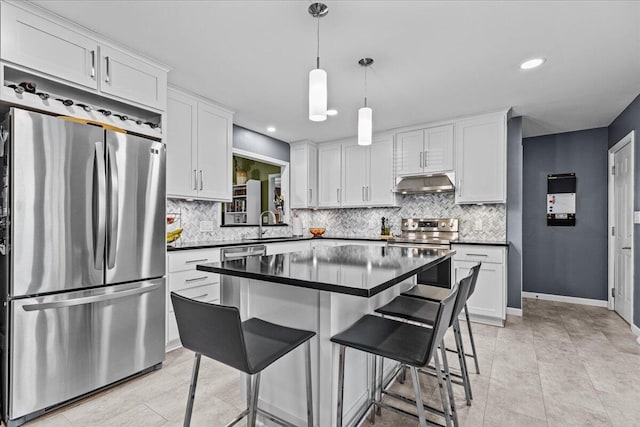 kitchen with under cabinet range hood, appliances with stainless steel finishes, white cabinetry, dark countertops, and tasteful backsplash