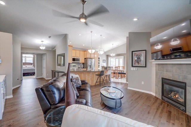 living area with a ceiling fan, wood finished floors, a fireplace, baseboards, and vaulted ceiling