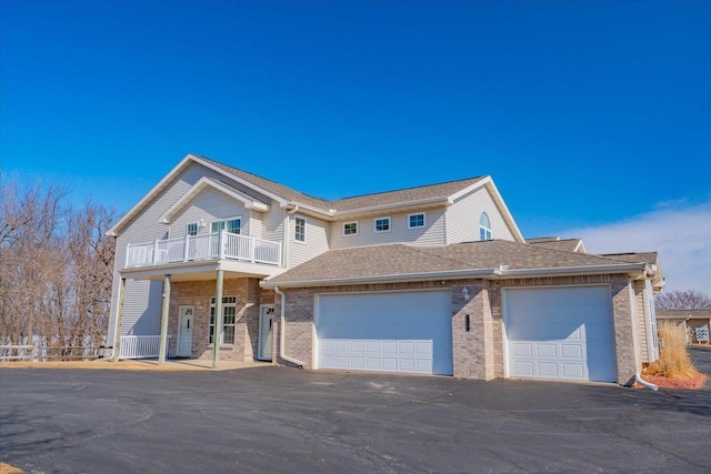 view of front of home featuring brick siding, roof with shingles, driveway, a balcony, and an attached garage