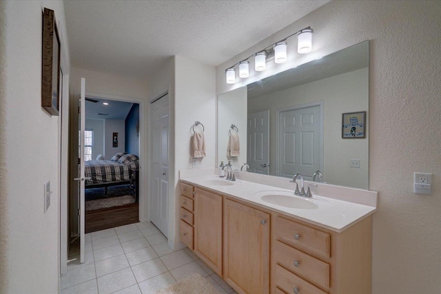 ensuite bathroom featuring a sink, a textured ceiling, double vanity, and tile patterned floors