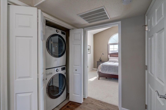 clothes washing area with wood finished floors, visible vents, laundry area, stacked washer and clothes dryer, and a textured ceiling