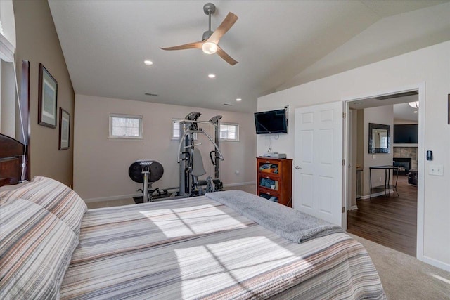 carpeted bedroom featuring baseboards, ceiling fan, lofted ceiling, a stone fireplace, and recessed lighting