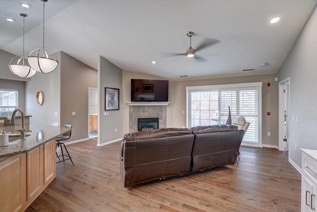 living room with visible vents, light wood-style floors, a fireplace, lofted ceiling, and ceiling fan