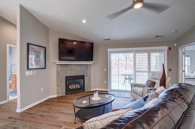 living area with visible vents, a tile fireplace, wood finished floors, baseboards, and vaulted ceiling