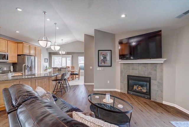 living room with visible vents, lofted ceiling, light wood-style flooring, and a tile fireplace