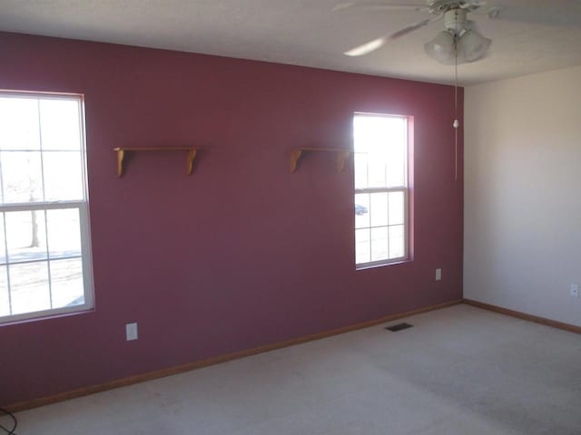 carpeted spare room featuring a ceiling fan, plenty of natural light, baseboards, and visible vents