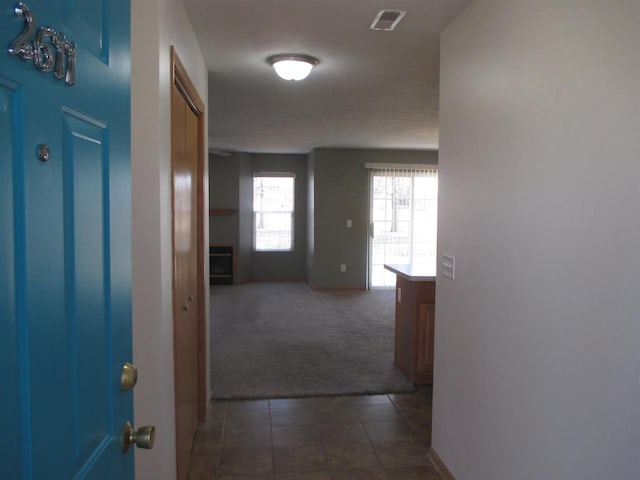 corridor featuring dark colored carpet, visible vents, baseboards, and dark tile patterned flooring