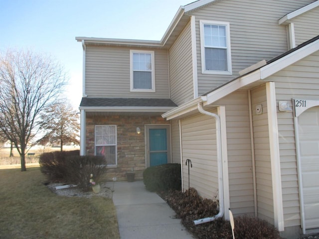 view of exterior entry featuring stone siding, a garage, and roof with shingles