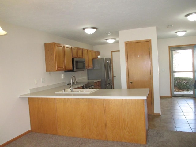 kitchen with appliances with stainless steel finishes, light countertops, a peninsula, and a sink