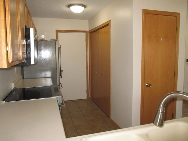 kitchen featuring light countertops, dark tile patterned flooring, brown cabinetry, and a sink