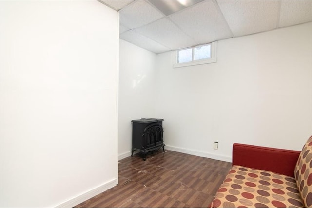 unfurnished room featuring a drop ceiling, baseboards, dark wood finished floors, and a wood stove