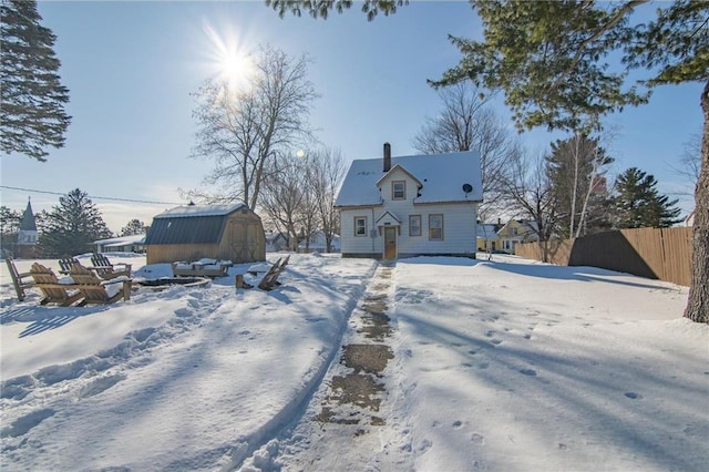 snow covered back of property with an outdoor structure, a storage unit, fence, and a chimney