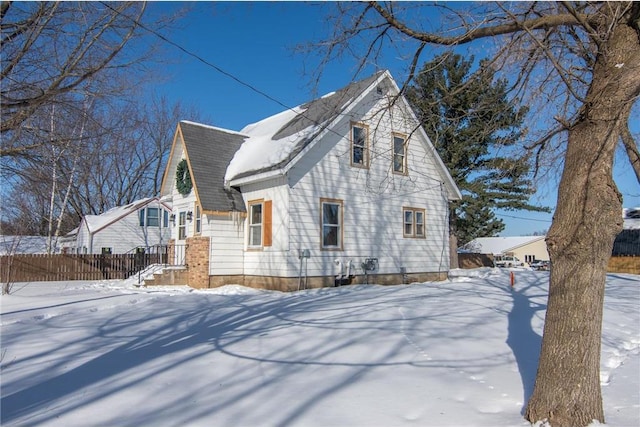 view of snowy exterior with a shingled roof and fence