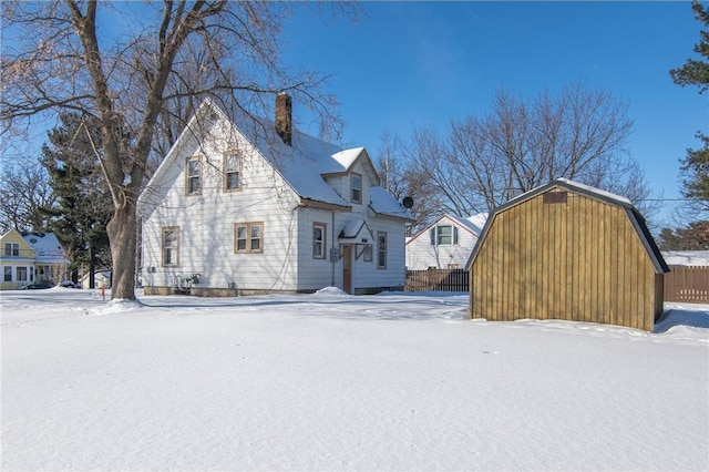 view of snow covered exterior with a gambrel roof, a chimney, and fence