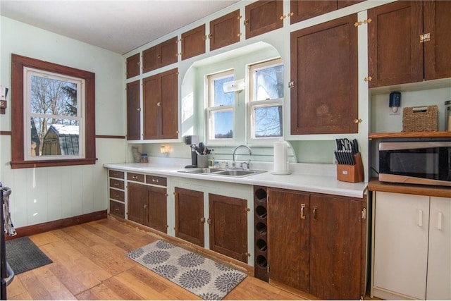 kitchen with baseboards, light wood-style flooring, a sink, light countertops, and stainless steel microwave