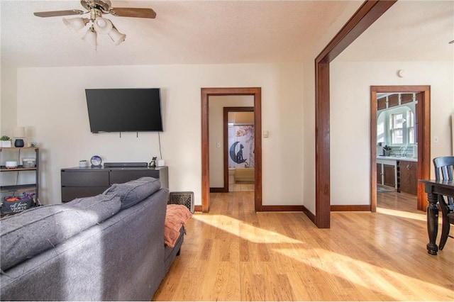 living area featuring a textured ceiling, light wood-style flooring, baseboards, and ceiling fan