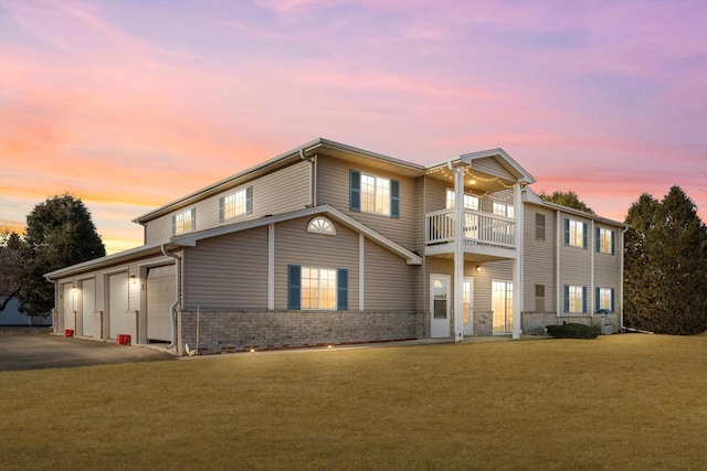 view of front of house featuring a balcony, an attached garage, a lawn, and brick siding