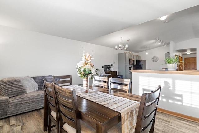 dining room featuring baseboards, light wood-style floors, an inviting chandelier, and vaulted ceiling