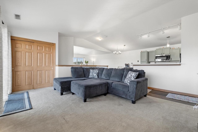 living area featuring visible vents, track lighting, vaulted ceiling, light carpet, and an inviting chandelier