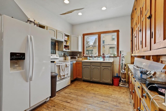 kitchen featuring light wood-style flooring, a sink, backsplash, recessed lighting, and white appliances