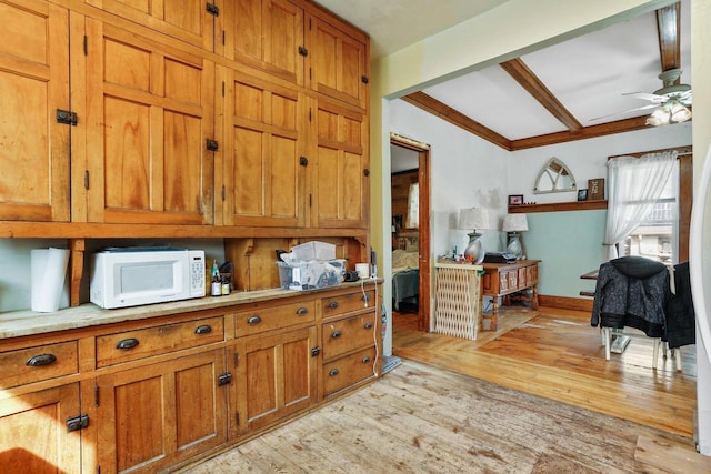 kitchen with beamed ceiling, light wood-style flooring, a ceiling fan, brown cabinetry, and white microwave