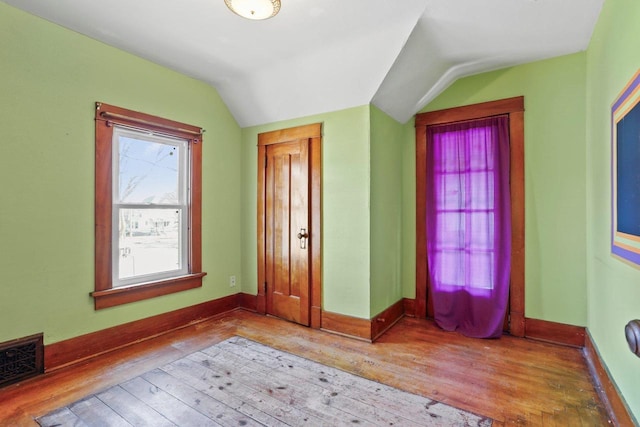 unfurnished bedroom featuring visible vents, wood-type flooring, baseboards, and vaulted ceiling