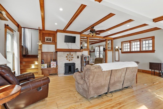 living room with stairs, beam ceiling, light wood-style flooring, and a brick fireplace