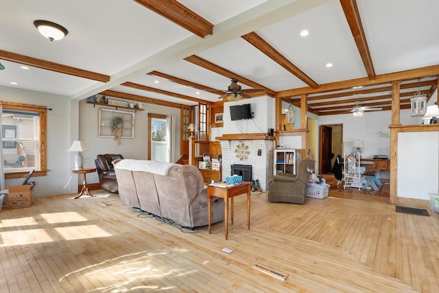 living area featuring beam ceiling, a brick fireplace, a ceiling fan, and hardwood / wood-style flooring