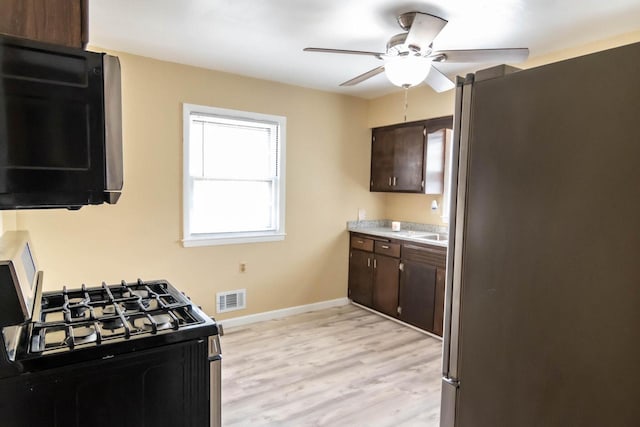 kitchen with visible vents, freestanding refrigerator, light countertops, dark brown cabinetry, and gas range