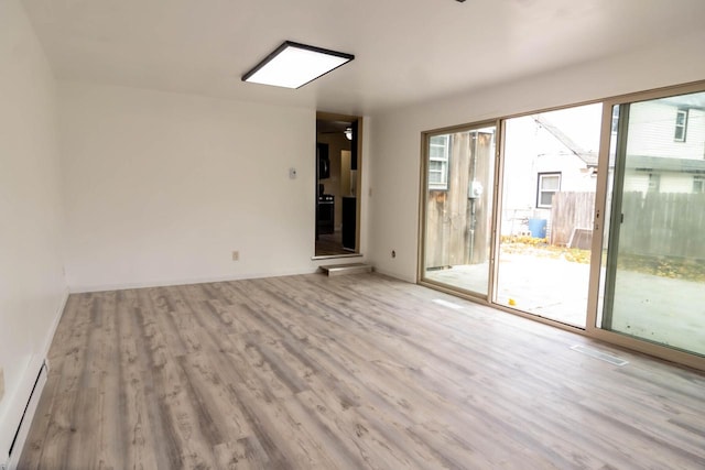 empty room featuring visible vents, wood finished floors, baseboards, and a baseboard radiator