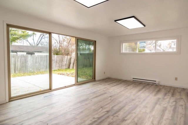 spare room featuring a baseboard heating unit, visible vents, wood finished floors, and baseboards