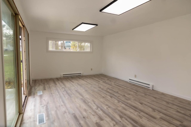 empty room featuring a baseboard heating unit, wood finished floors, visible vents, and baseboards