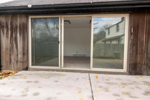 entrance to property with a patio area, baseboard heating, and a shingled roof