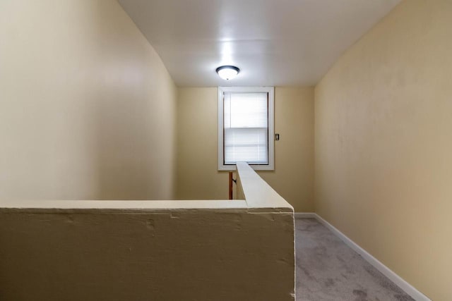 corridor featuring light carpet, an upstairs landing, and baseboards