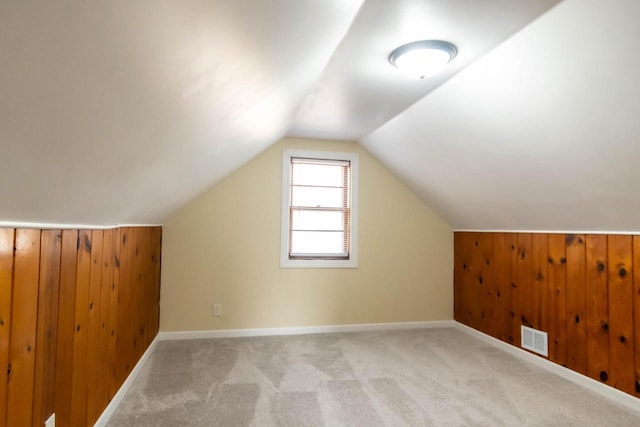 additional living space featuring visible vents, baseboards, wood walls, vaulted ceiling, and carpet floors