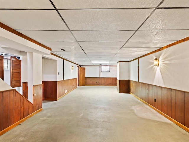 below grade area with a wainscoted wall, a paneled ceiling, and wooden walls