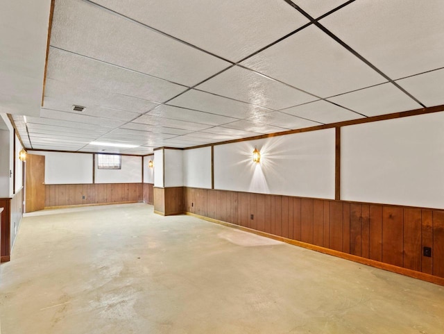 below grade area featuring visible vents, a paneled ceiling, wooden walls, and wainscoting