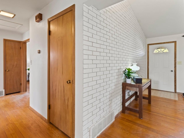 foyer entrance featuring light wood finished floors, visible vents, brick wall, and lofted ceiling