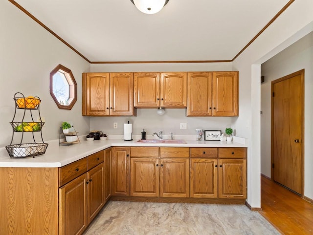 kitchen with a sink, ornamental molding, brown cabinetry, and light countertops