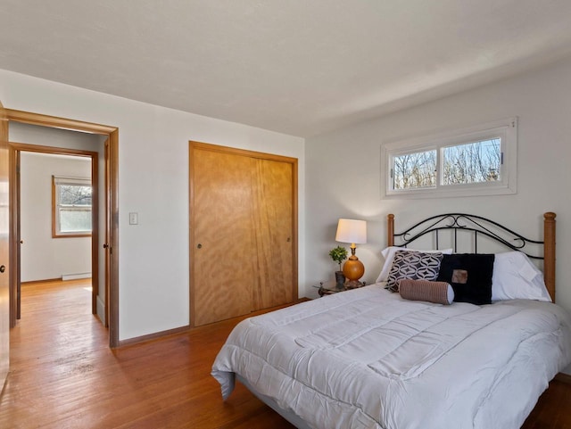 bedroom with light wood finished floors, baseboard heating, baseboards, and a closet