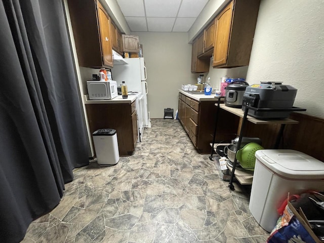 kitchen featuring brown cabinets, stone finish flooring, light countertops, and a paneled ceiling