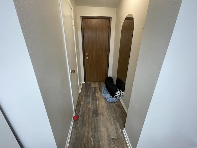 hallway featuring wood finished floors, arched walkways, and baseboards