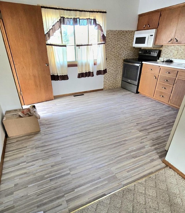 kitchen featuring visible vents, brown cabinets, light wood-style flooring, stainless steel electric stove, and white microwave