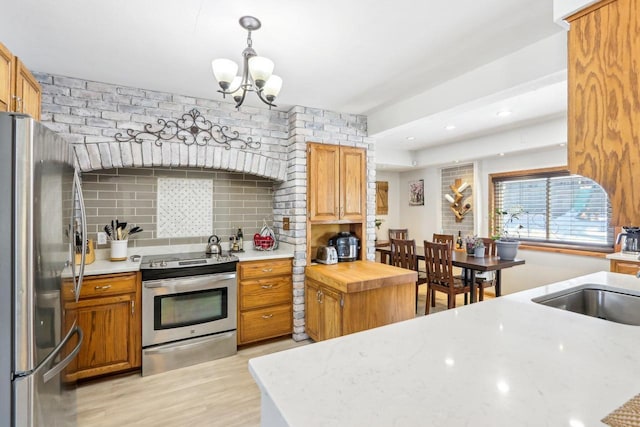 kitchen featuring backsplash, appliances with stainless steel finishes, light wood-style floors, a notable chandelier, and a sink