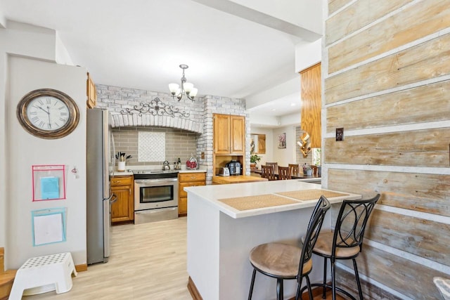 kitchen with backsplash, appliances with stainless steel finishes, a breakfast bar area, light countertops, and a chandelier