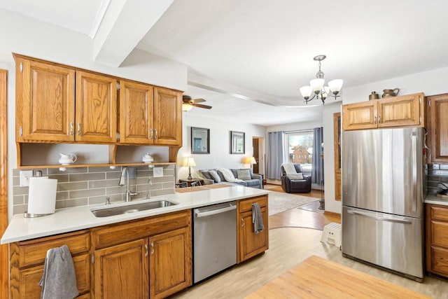 kitchen with light countertops, decorative backsplash, appliances with stainless steel finishes, light wood-style floors, and a sink