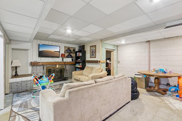 living area with a drop ceiling, concrete block wall, a brick fireplace, and concrete floors